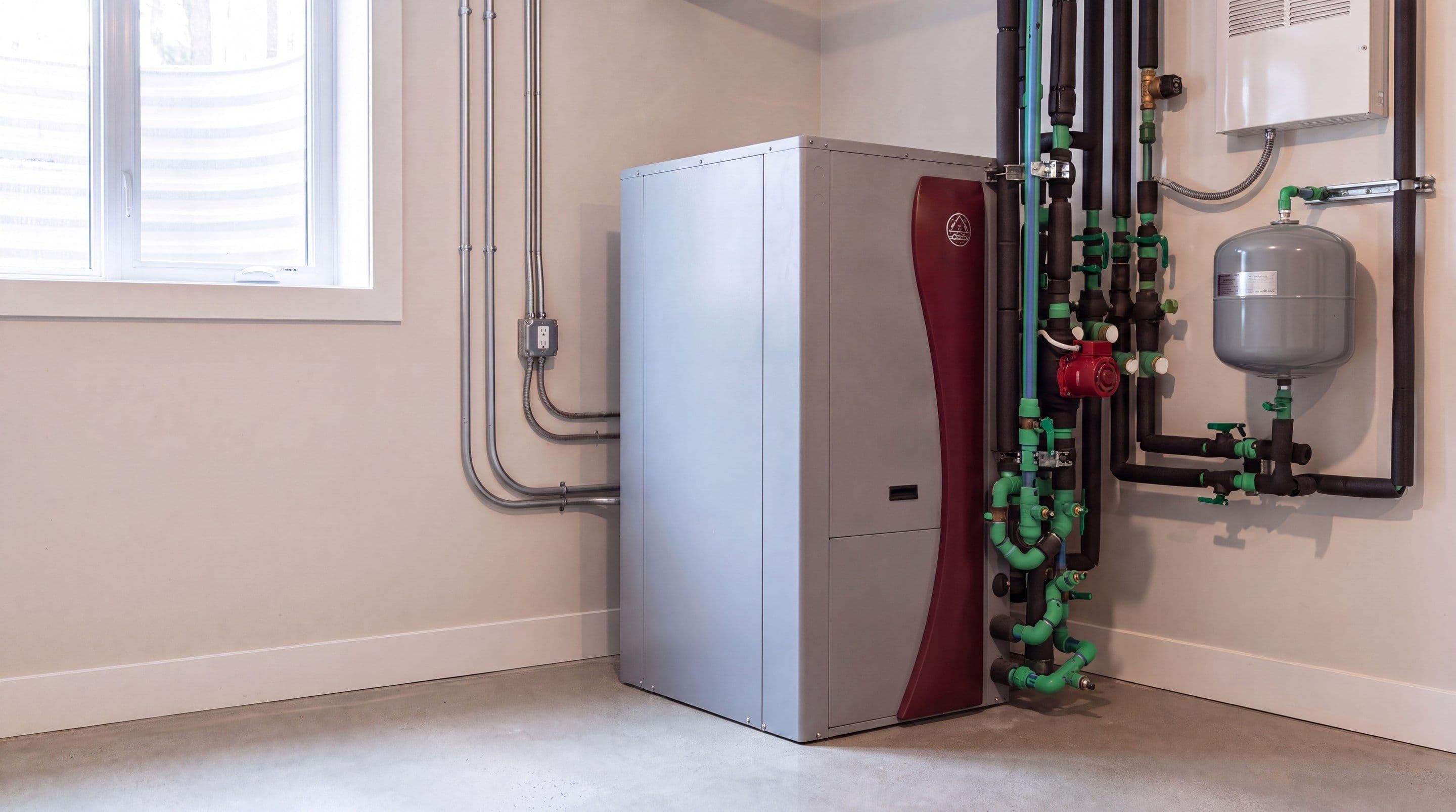 Une thermopompe géothermique installée dans une salle mécanique au sous-sol avec son collecteur de tuyauterie